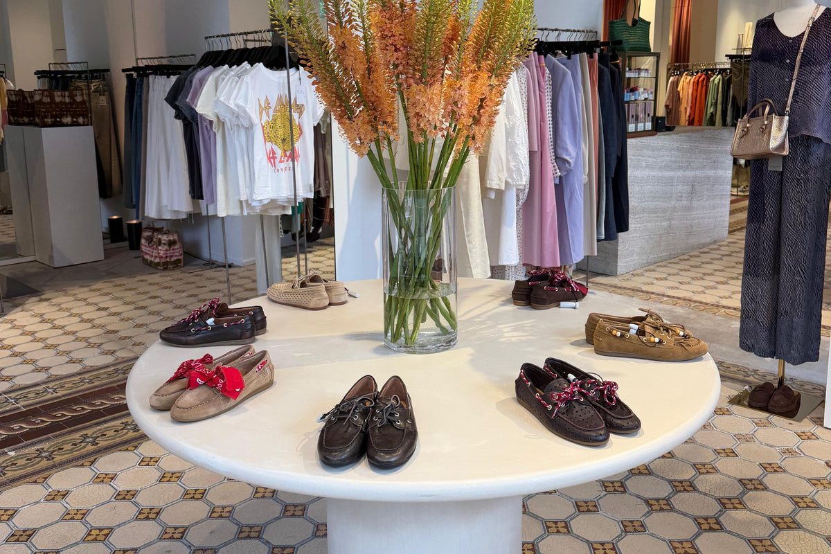 Intérieur de la boutique Kelly Shop, place Georges Brugmann à Ixelles : table ronde avec les mocassins de la saison, portants et carreaux de ciment